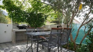 An outdoor patio with a table and chairs, a grill, and a view of a garden and a building in the background. - Apartments Relax Brela - Two Bedroom Apartment (Brela)