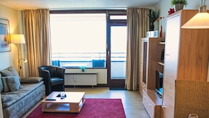 Un salon moderne comprenant un canapé, un fauteuil, une table basse et une table à manger avec des couverts et un verre.