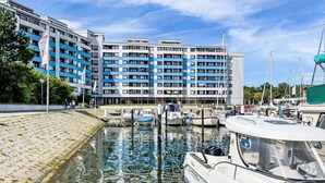 Un port de plaisance avec des bateaux amarrés, un bâtiment à la façade bleue et blanche, et un ciel dégagé.