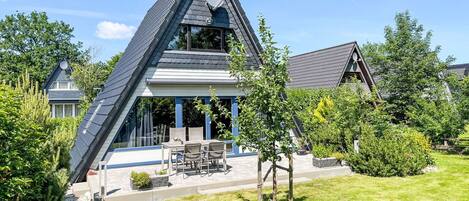 A modern house with a sloped roof, a covered patio with outdoor furniture, and a well-maintained lawn.