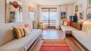 Ein gemütliches Zimmer mit zwei Sofas, einem Fernseher und einem großen Fenster mit Bergblick.