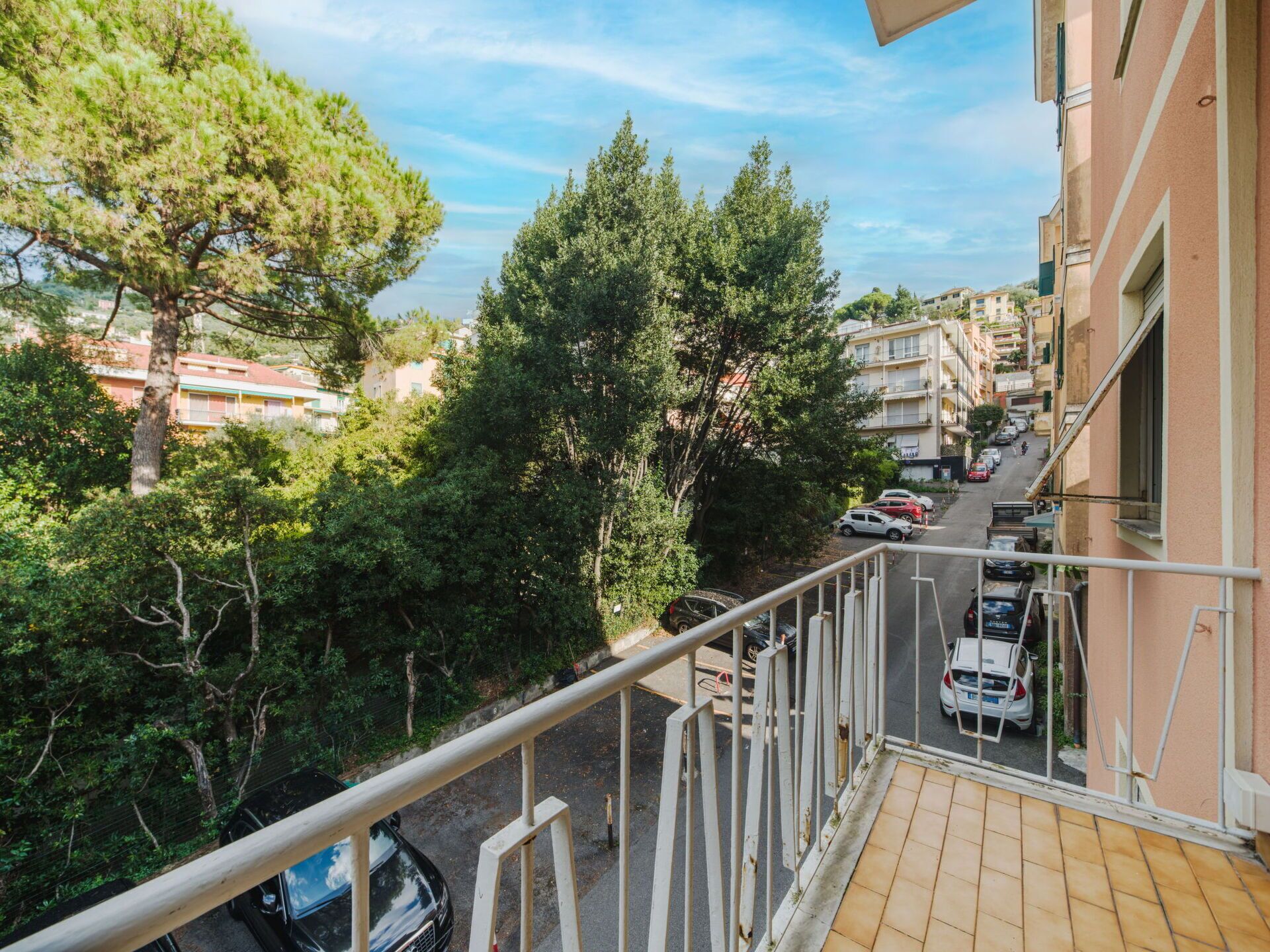 Un balcón con vistas a una calle, coches aparcados y edificios.