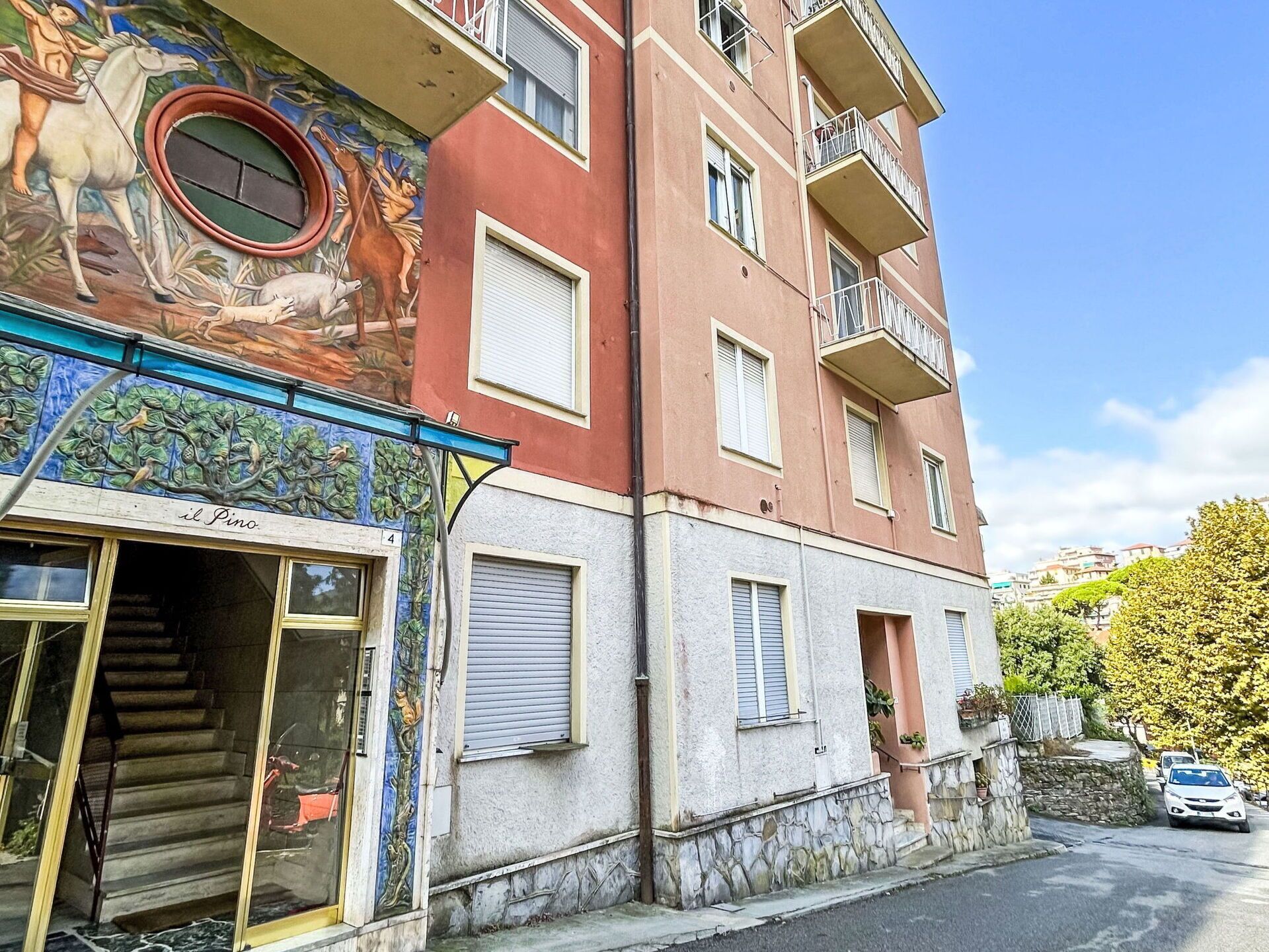 A multi-story building with a mural on the facade, a visible entrance, and a staircase leading to the entrance.