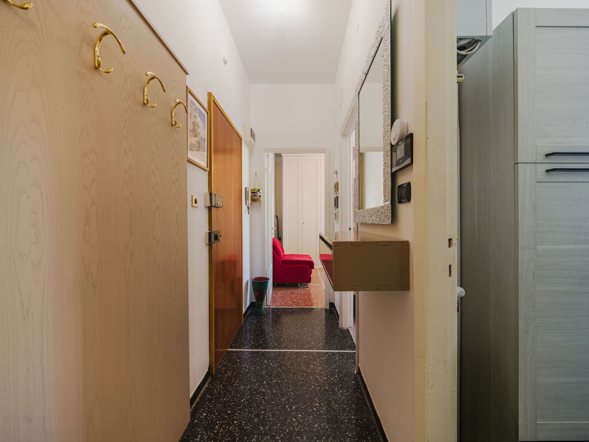 Un couloir avec une porte en bois, une chaise rouge et un meuble blanc.
