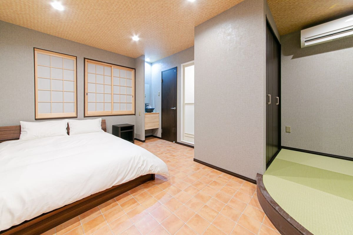 Habitación de hotel con cama, mesita de noche, espejo, armario y una puerta corredera que da al baño.