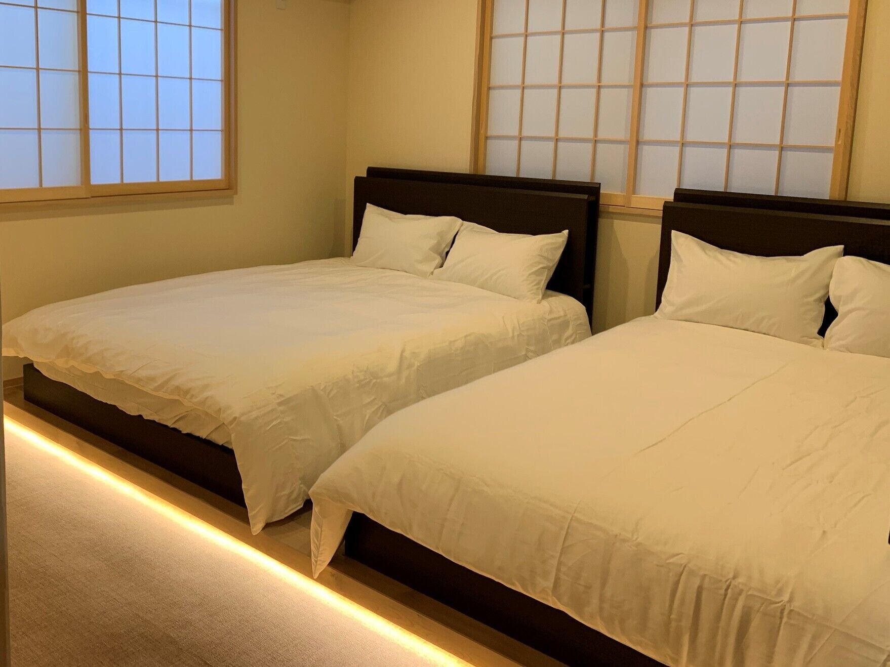 A hotel room with two beds, a wooden headboard, and a window with a grid pattern.