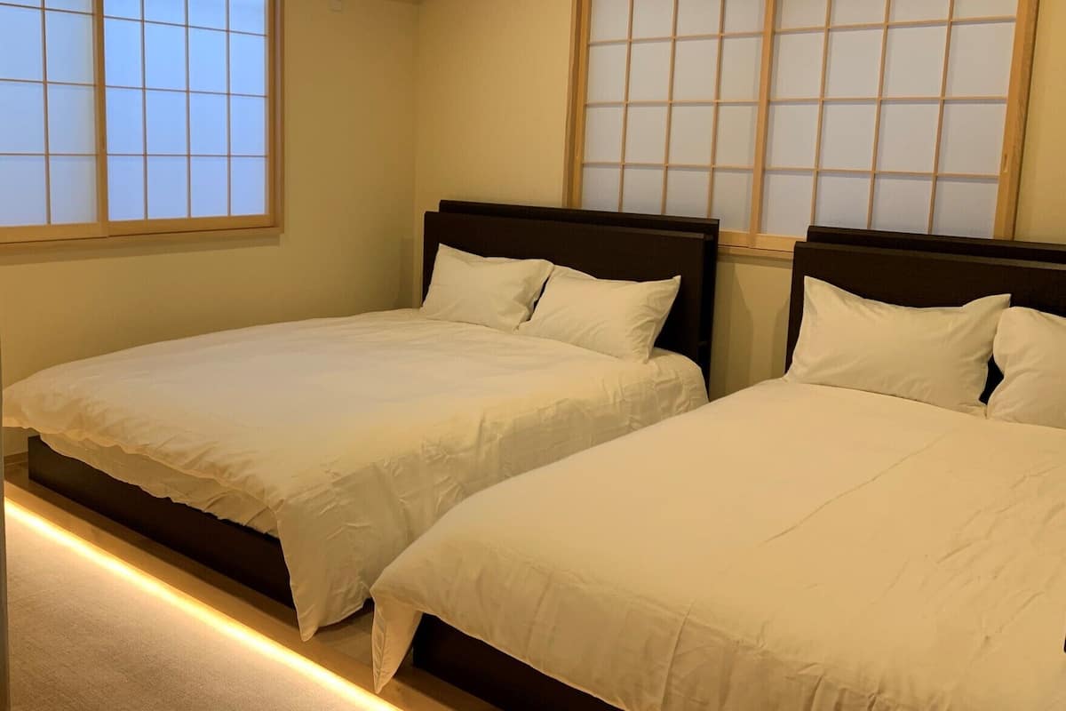 Habitación de hotel con dos camas, cabecero de madera y ventana con diseño de celosía.