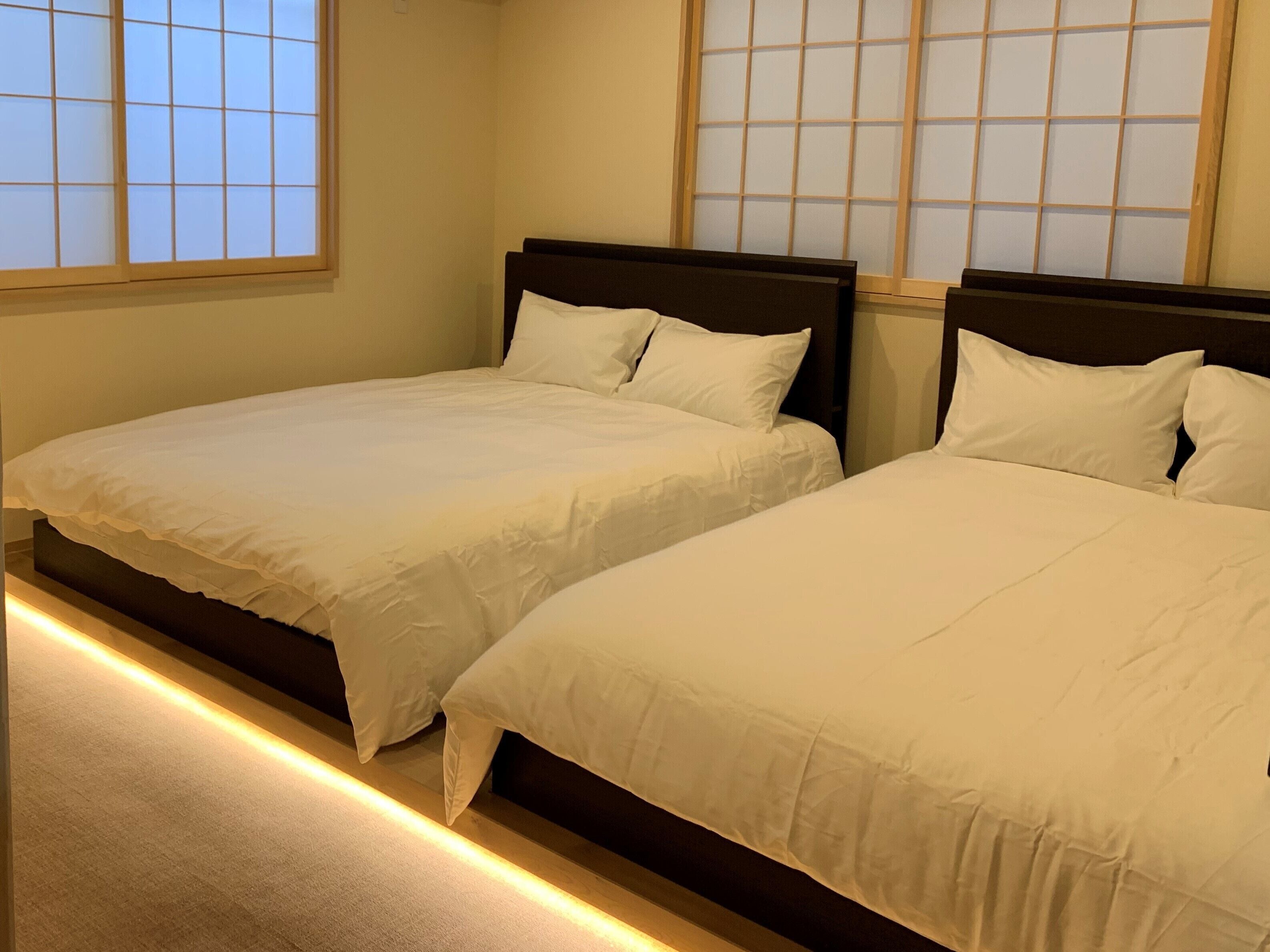 Two single beds with wooden headboards in a room with a view of a traditional Japanese window.