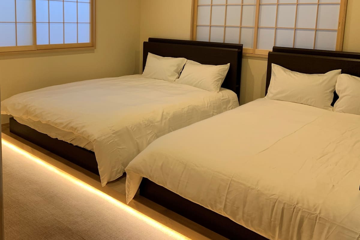 Dos camas individuales con cabeceros de madera en una habitación con vistas a una ventana tradicional japonesa.