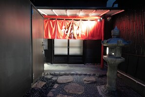Una entrada tradicional japonesa con un farol de piedra, un toldo rojo y una puerta de madera.