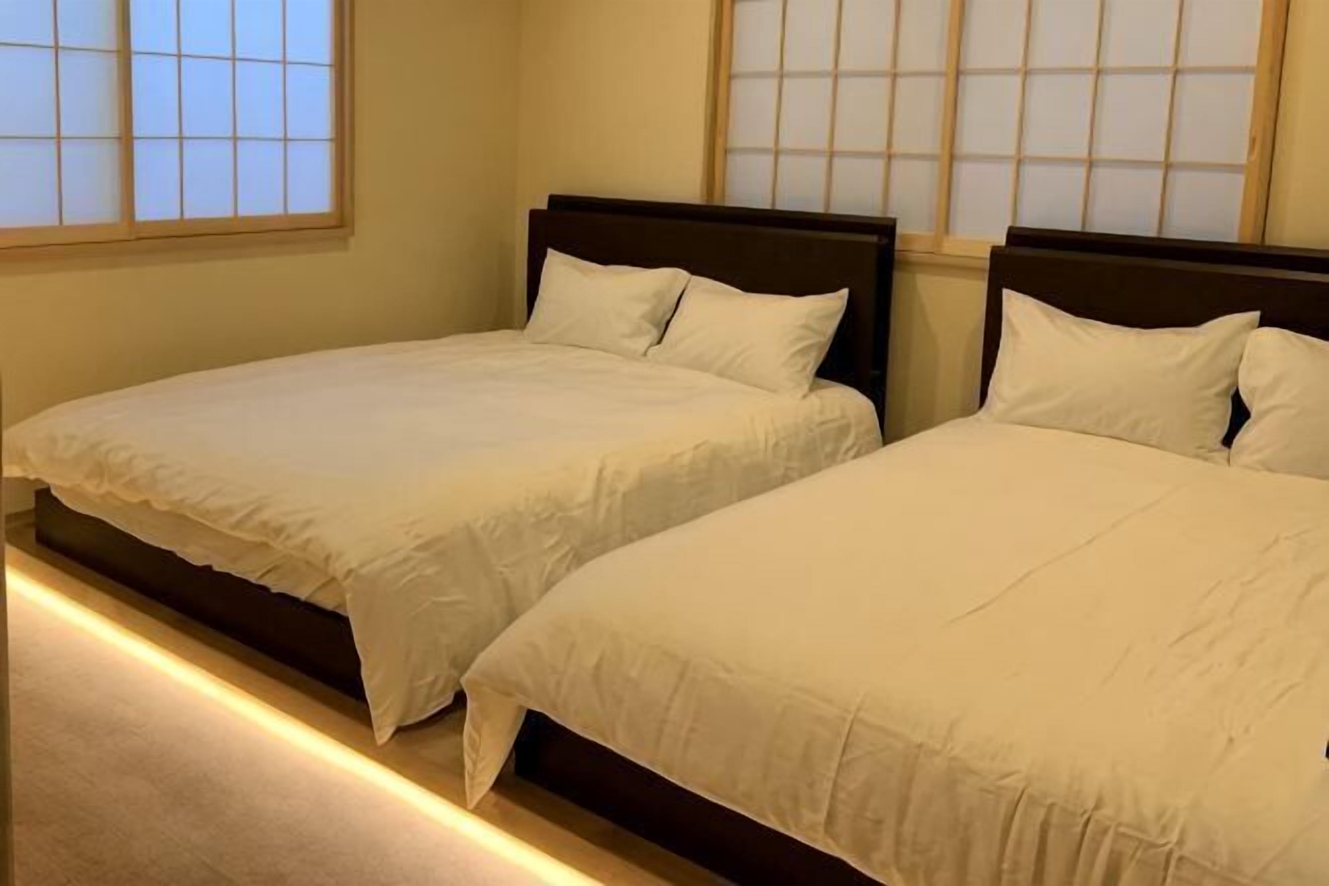 Two beds with wooden headboards in a room with large windows.