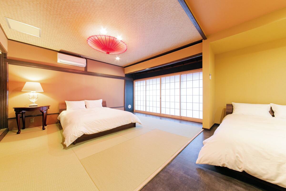 Habitación de hotel con dos camas, un tradicional panel japonés shoji, suelo de tatami y un ventilador de techo.