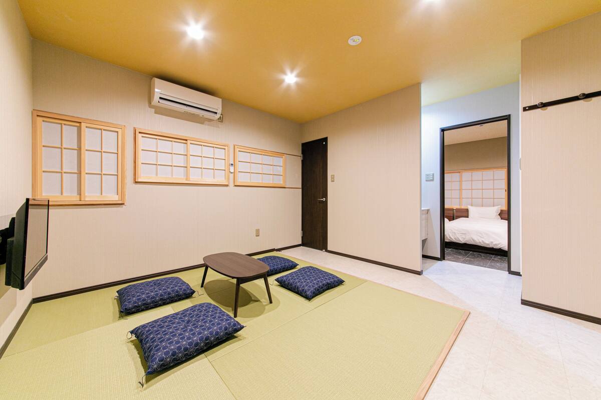 Una habitación con esteras de tatami, un futón, una pequeña mesa y un televisor.