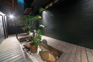 Una terraza de madera con un muro negro y una planta en maceta.