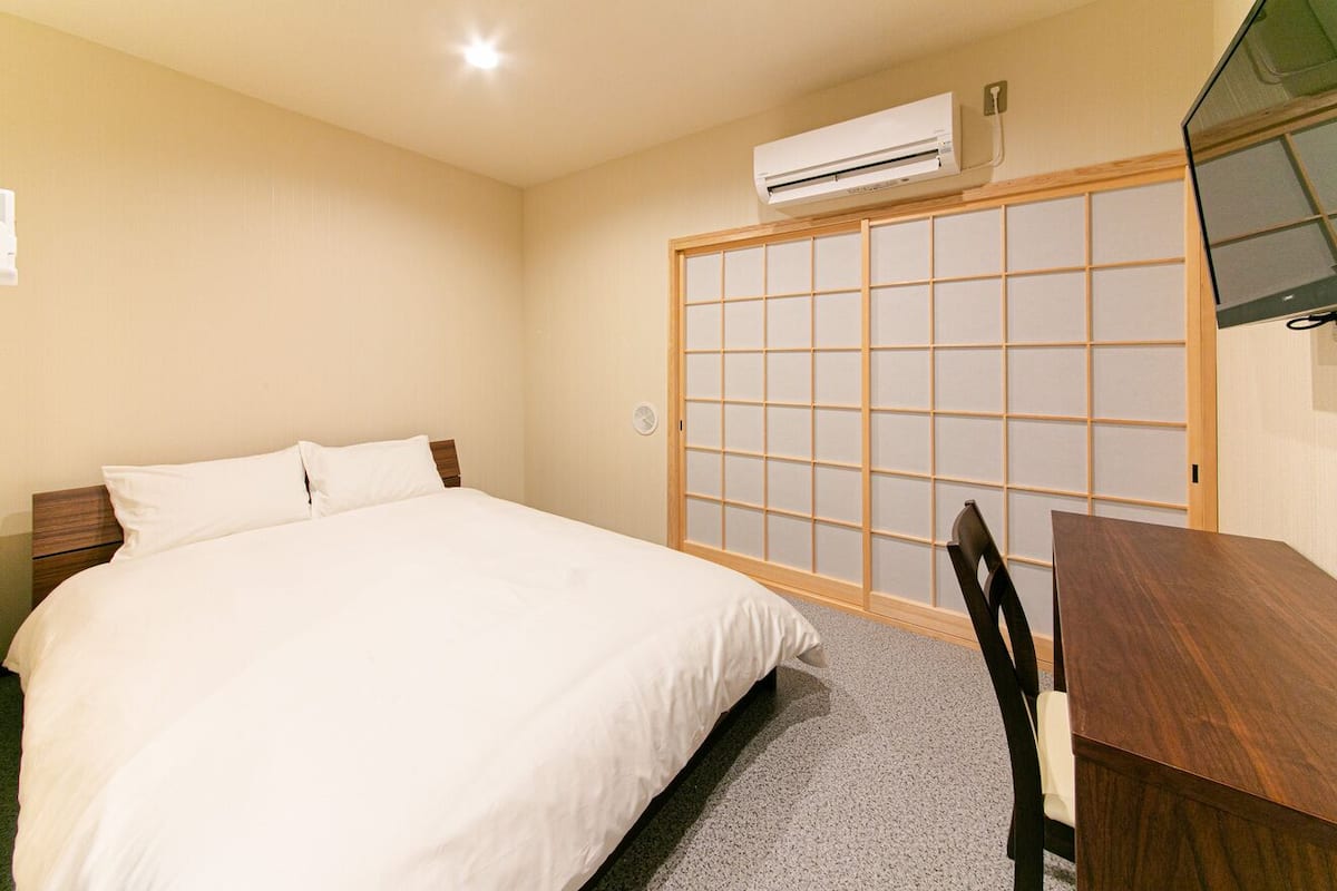 Habitación de hotel con cama, un escritorio de madera y una puerta corredera de tipo shoji.