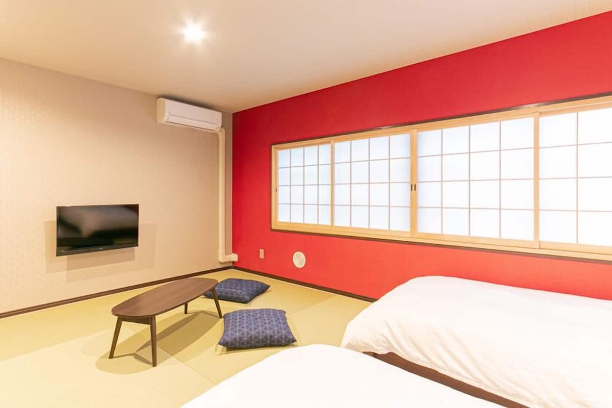 Una habitación con cama, un banco, televisión y un ventanal grande.