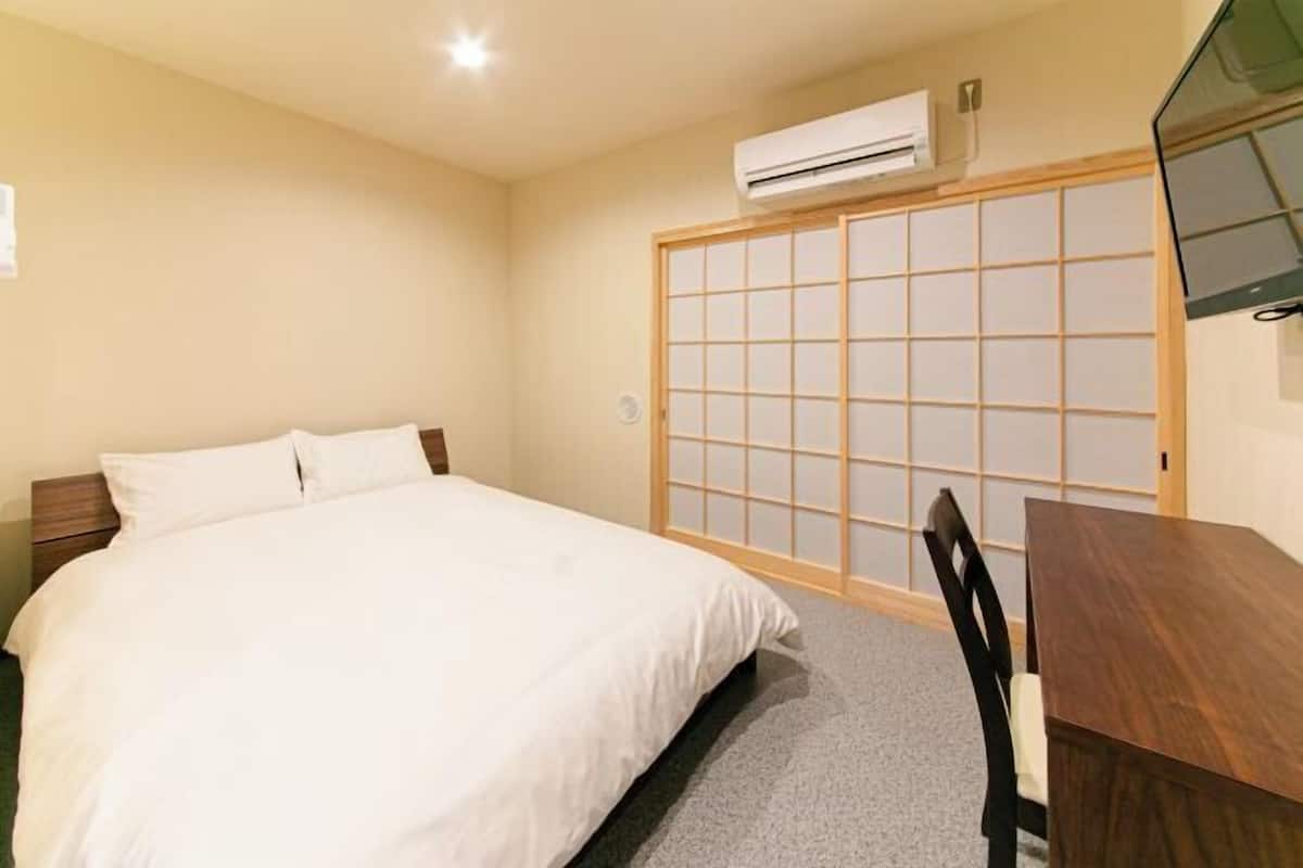 Habitación de hotel con cama, una mesa de madera, una silla, puerta corredera de tipo shoji y equipo de aire acondicionado.