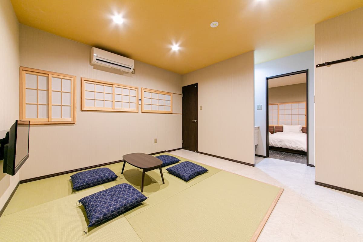 Una habitación con esteras de tatami, una mesa baja, cojines, una cama y un aire acondicionado.