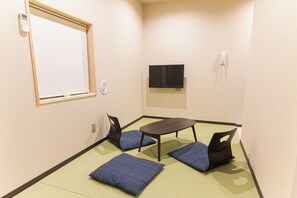 Una habitación pequeña con una pizarra, un televisor de pantalla plana, una mesa con sillas y piso de tatami japonés tradicional.