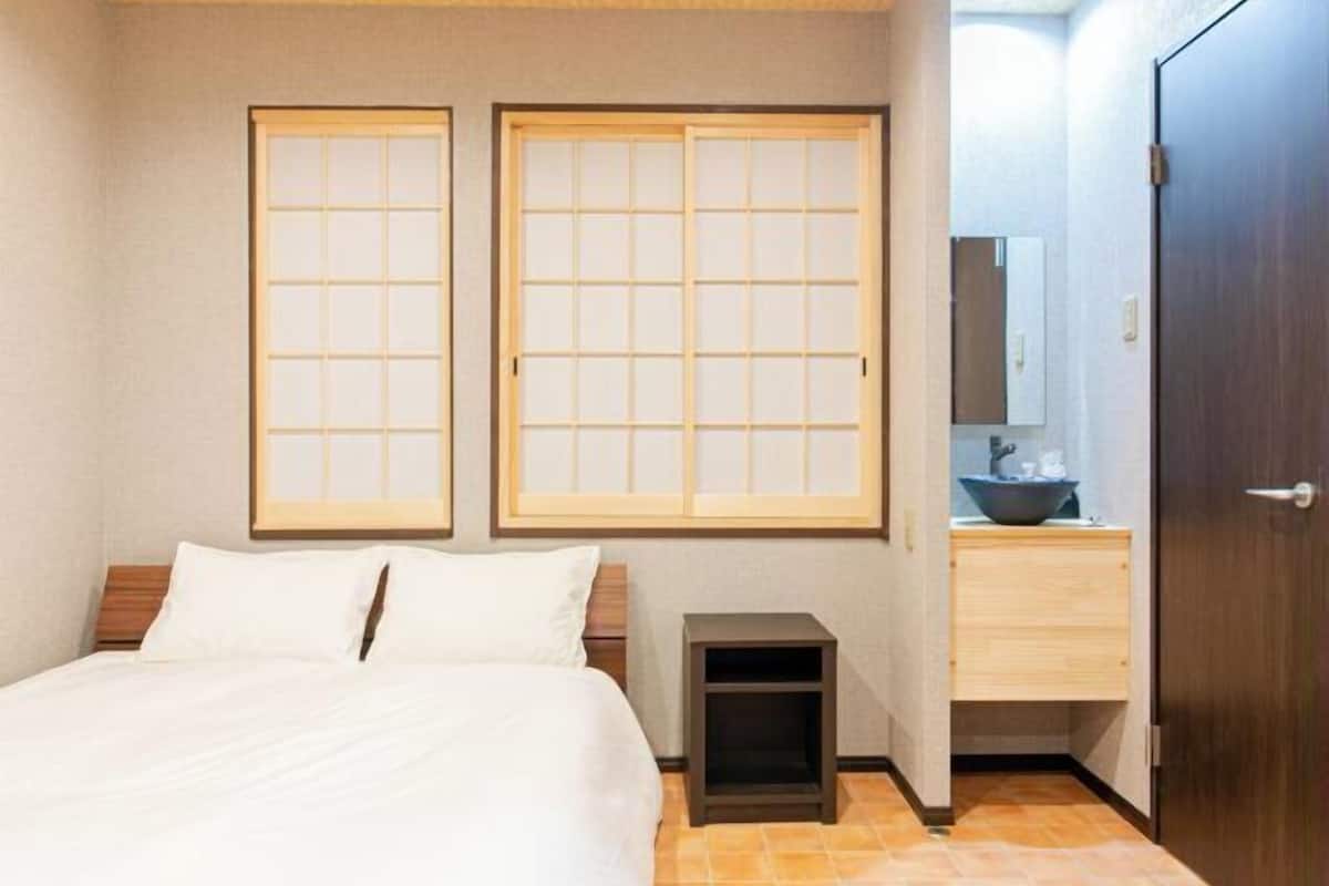 Habitación de hotel con una cama, dos puertas correderas, una mesita de noche pequeña, un armario de madera y un espejo.