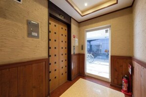 Rebedor d'hotel amb panells de fusta, un extintor i una porta que dóna a l'exterior.