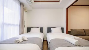 Habitación de hotel con dos camas individuales, un sofá y un ventanal grande con cortinas.