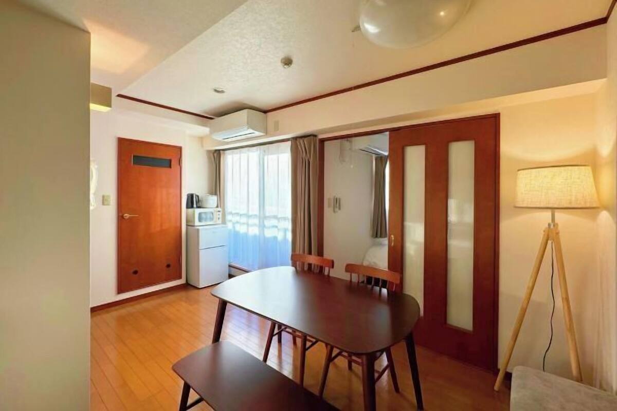 Un comedor con mesa y bancos de madera, una kitchenette y una lámpara.