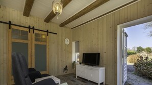 A room with wooden walls, a ceiling fan, a TV on a white cabinet, and a door leading outside.