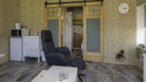 A cozy room with wooden walls, a black office chair, a small white desk, a microwave, and a clock on the wall.