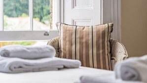 A room with a wicker chair, a striped pillow, and neatly folded towels on a bed. - Nice apartment for 4 guests with TV (Mevagissey)
