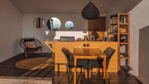Un espace de vie compact comprenant une table à manger en bois, quatre chaises, un petit coin cuisine et une bibliothèque intégrée.