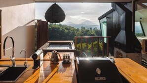 Une cuisine moderne dotée d’un barbecue intégré, d’un luminaire suspendu et offrant une vue sur un paysage boisé.