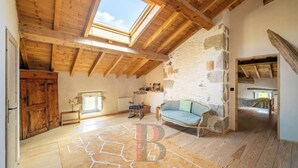 A spacious loft with exposed wooden beams, a stone wall, and a cozy seating area with a blue sofa. - Large renovated house, ideal for a large family looking for peace and quiet. (Fargues-sur-Ourbise)