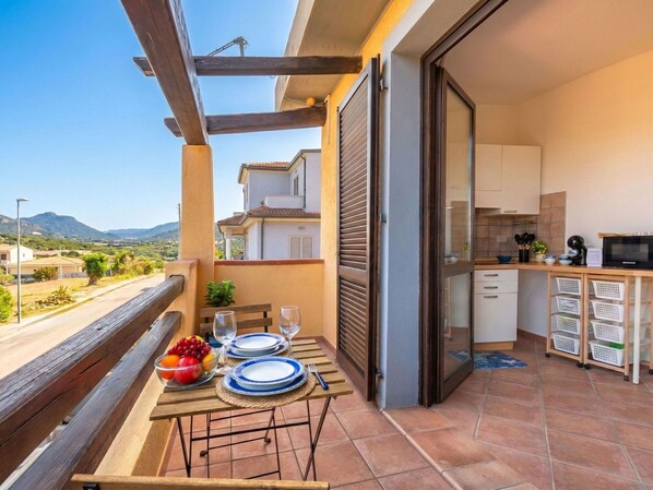 A balcony with a table set for two, a bowl of fruit, and a view of the surrounding area.