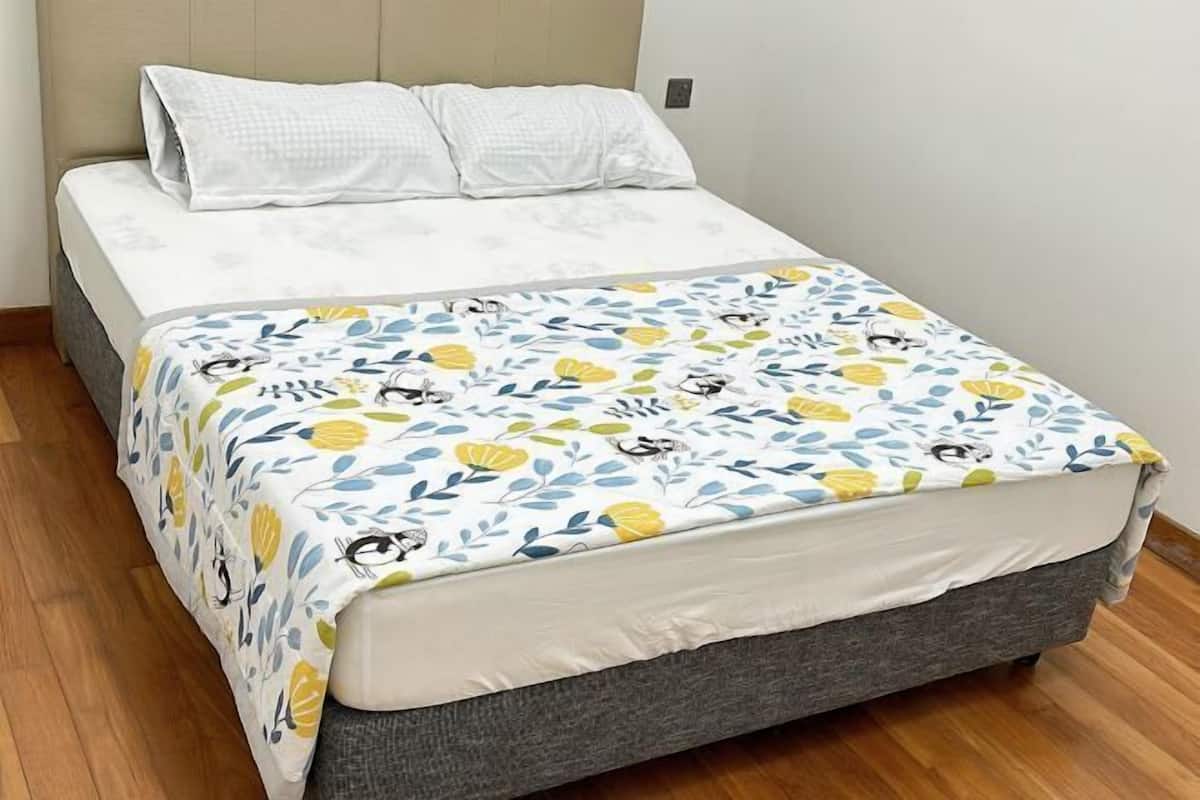 A bed with a floral-patterned bedspread, a grey upholstered headboard, and white pillows.