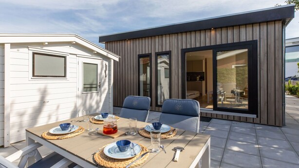 A dining area with a table set for four, two chairs, and a modern building with large windows in the background. - Wonderful private villa for 4 people with WIFI, TV and terrace (Veere)