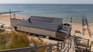 A beachside building with a flat roof, solar panels, and a wooden deck leading to the beach. - Wonderful private villa for 4 people with WIFI, TV and terrace (Veere)