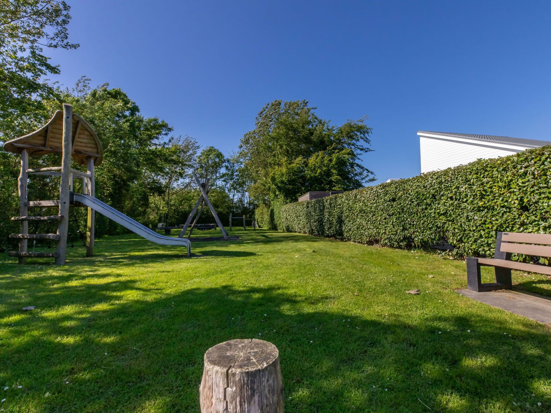 Ein Spielplatz mit Rutsche und Schaukeln, umgeben von einem gepflegten Rasen und einer Hecke.