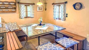 Un comedor con una mesa de vidrio, bancos, cojines estampados y adornos florales.
