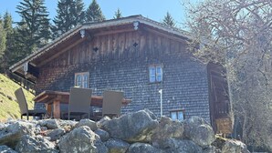 Una cabaña de madera con techo inclinado, ventanas amplias y un muro de piedra al frente.