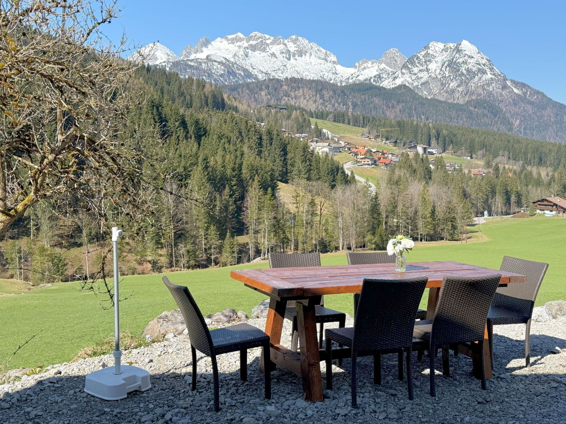 Een eettafel met stoelen buiten, met uitzicht op een berglandschap en een dorp in de verte.