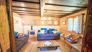 Una habitación acogedora de estilo cabaña, con techo de madera, un sofá con cojines, una mesita pequeña y un sillón de mimbre.