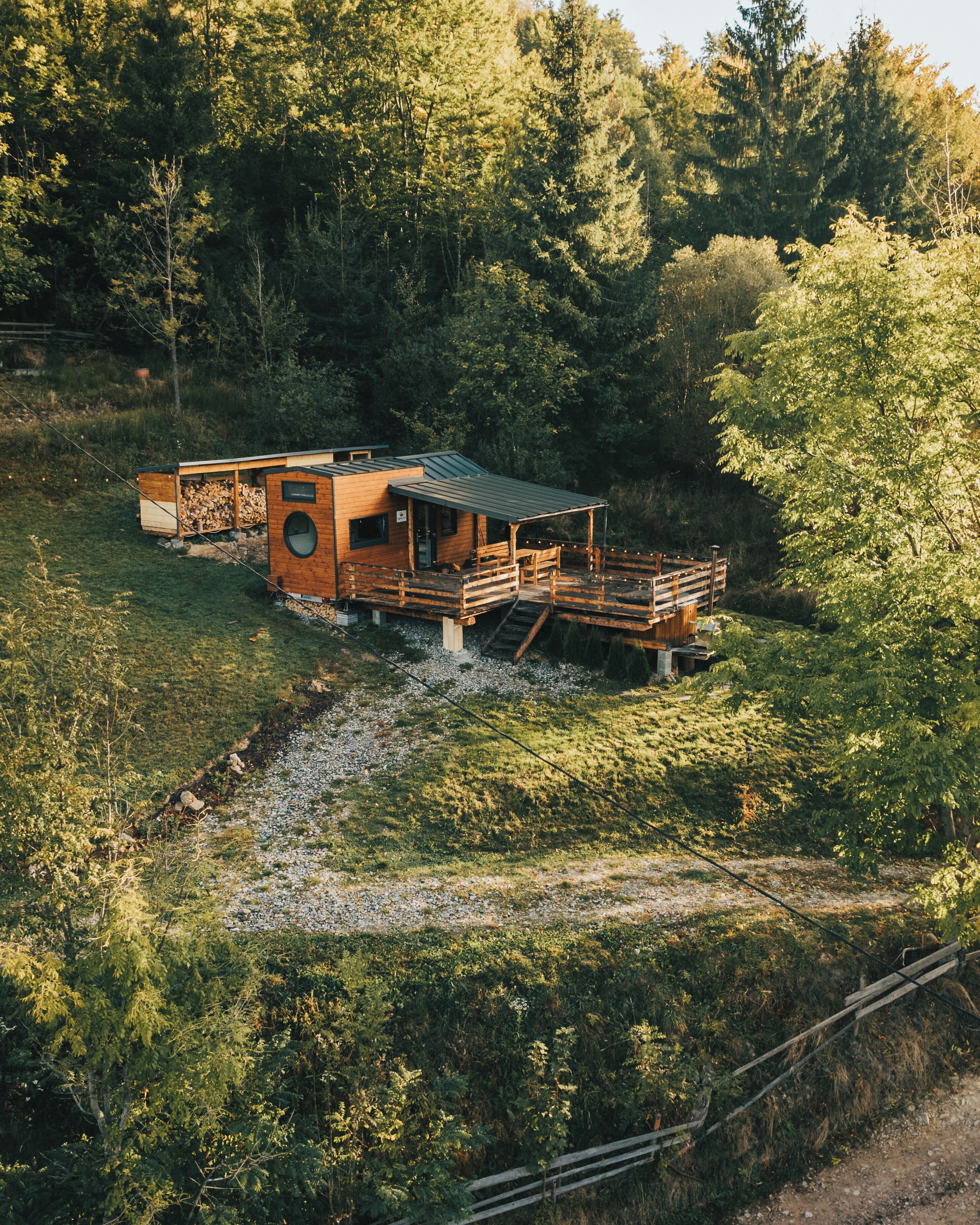 Een houten vakantiehuis met terras en overdekt gedeelte, omgeven door een dicht bos.