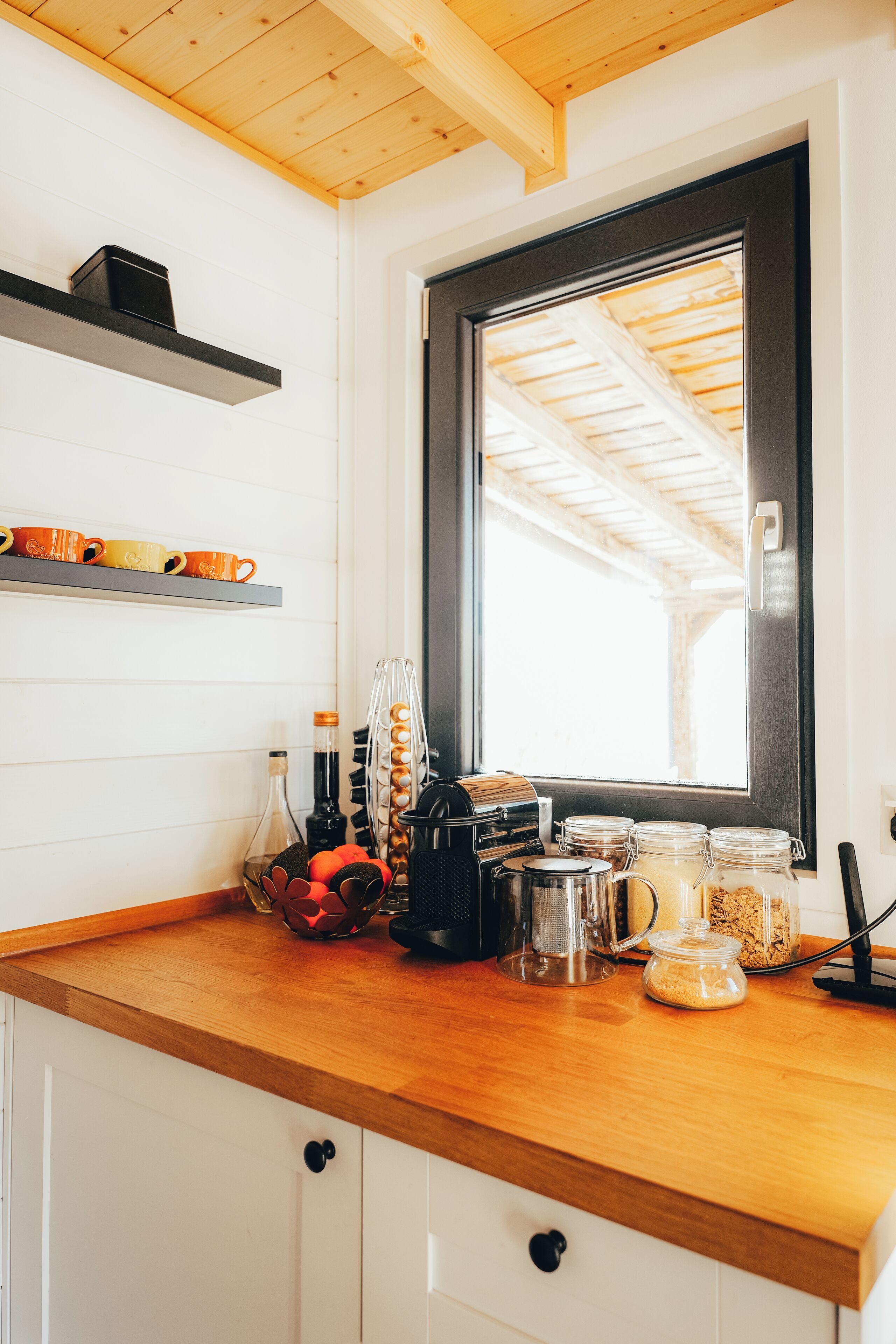 A kitchen with a wooden countertop, a window with a view of the roof, and various kitchen items like a coffee maker and jars.