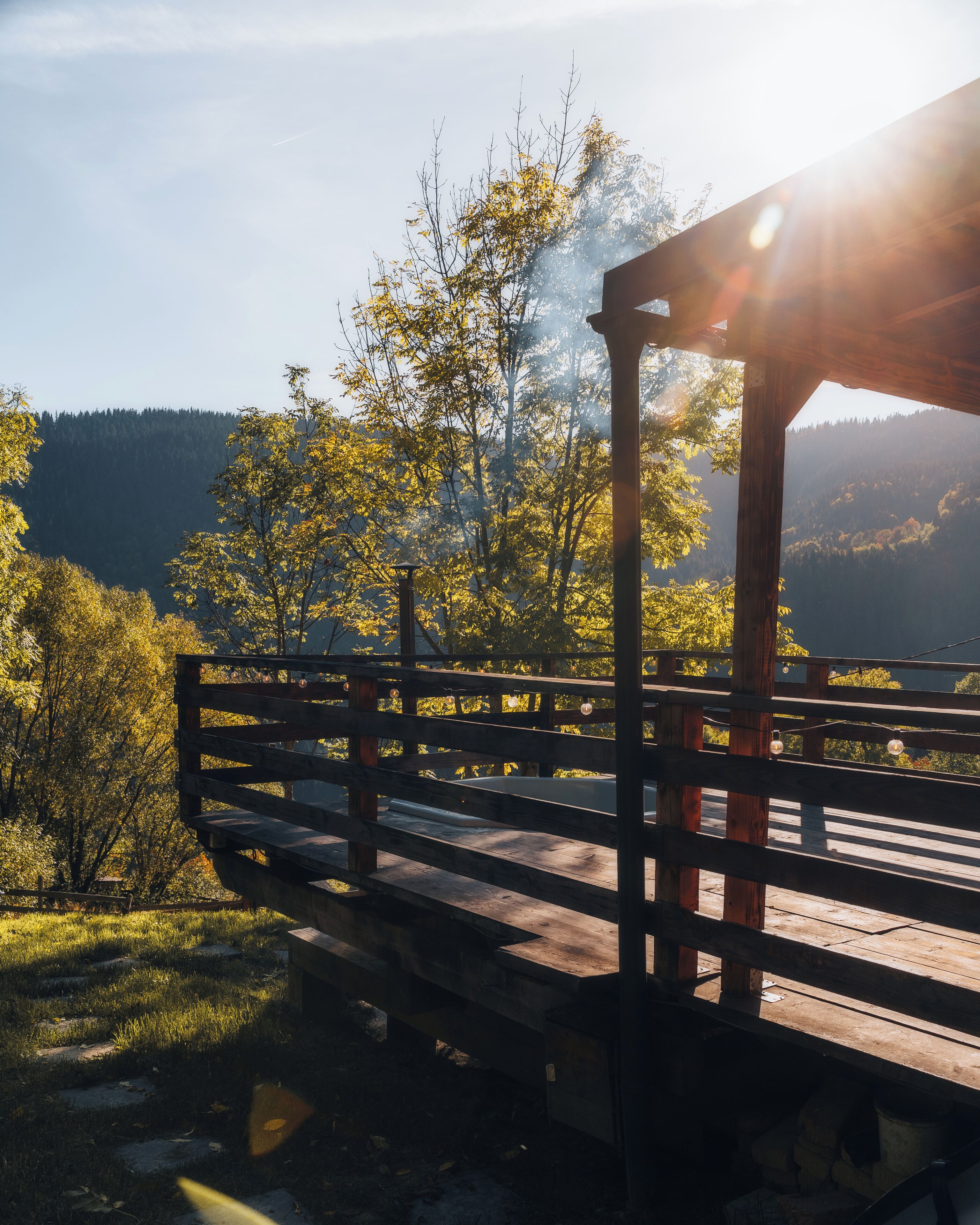 Une terrasse en bois offrant une vue sur une vallée boisée et, au loin, sur une chaîne de montagnes.