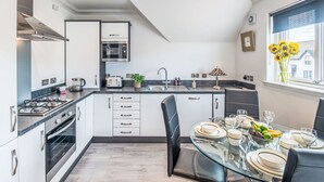 A modern kitchen with a gas stove, oven, and microwave. There is a dining table with chairs and a window with a view of buildings.