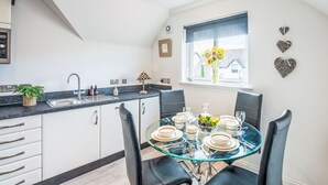 A modern kitchen with a dining area, featuring a glass table set for six, white cabinets, and a window with a view of the outside.