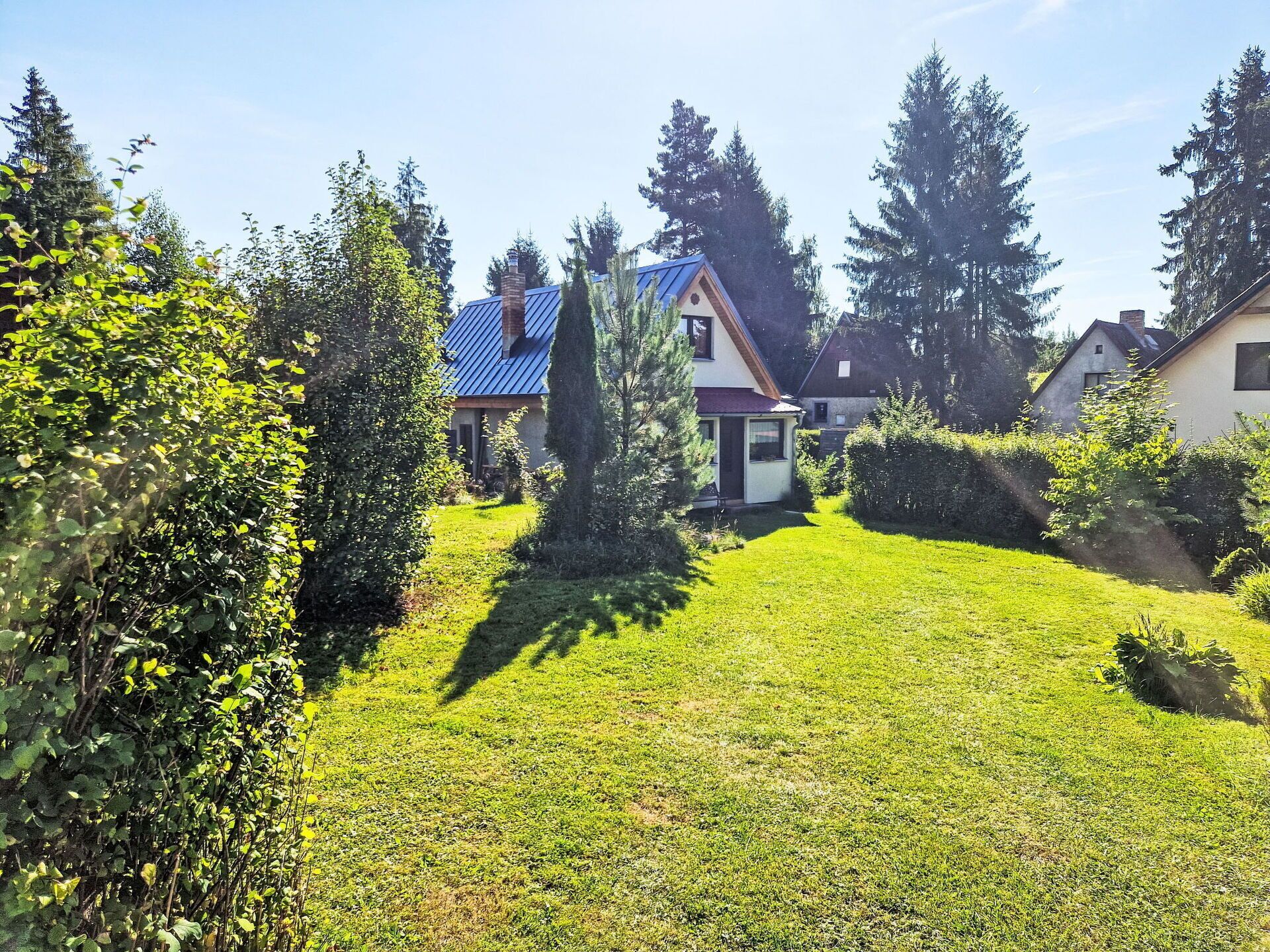 A residential area with houses, a well-maintained lawn, and surrounding trees.
