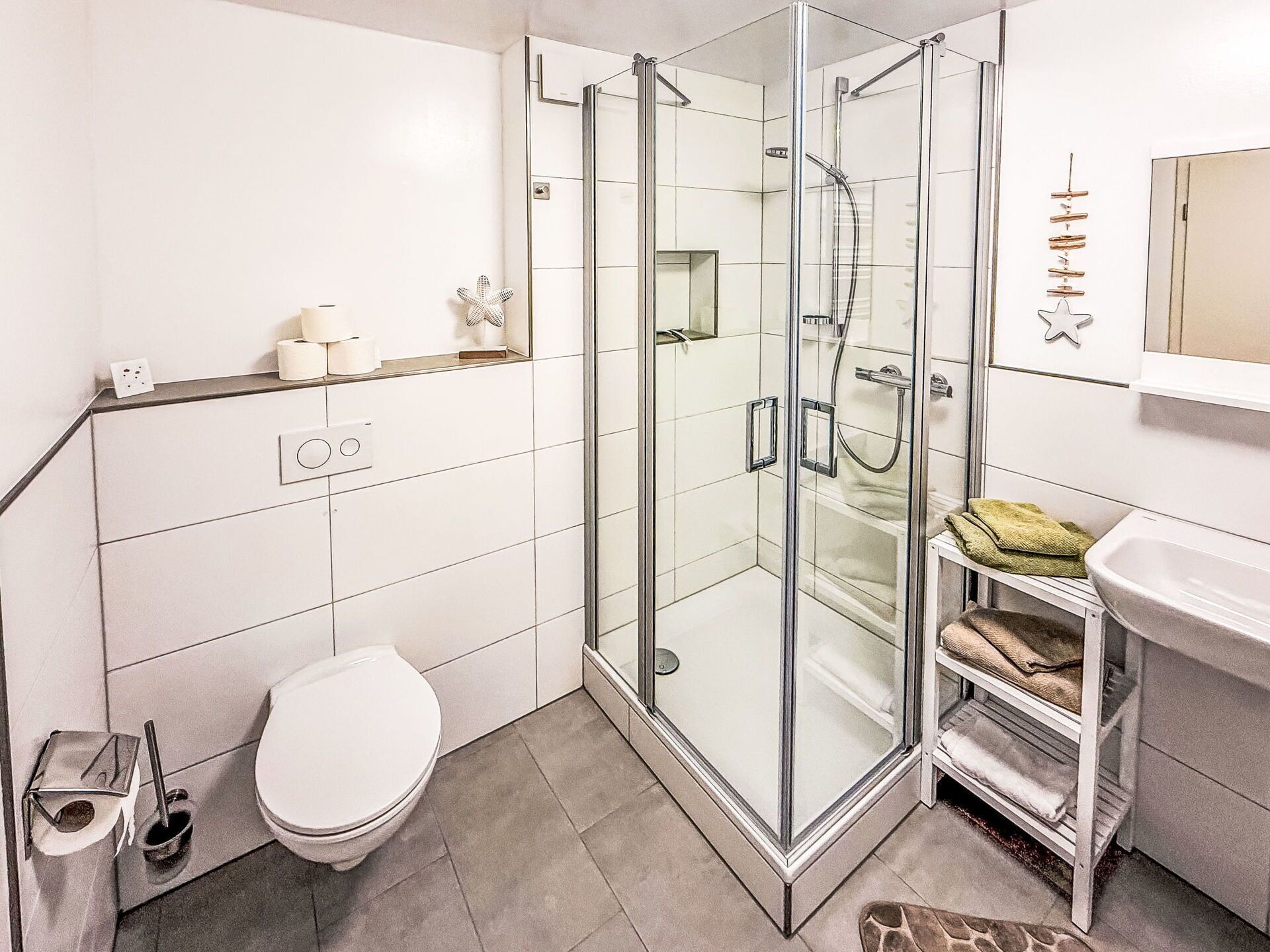 A modern bathroom with a glass-enclosed shower, a toilet, and a sink with a towel rack.