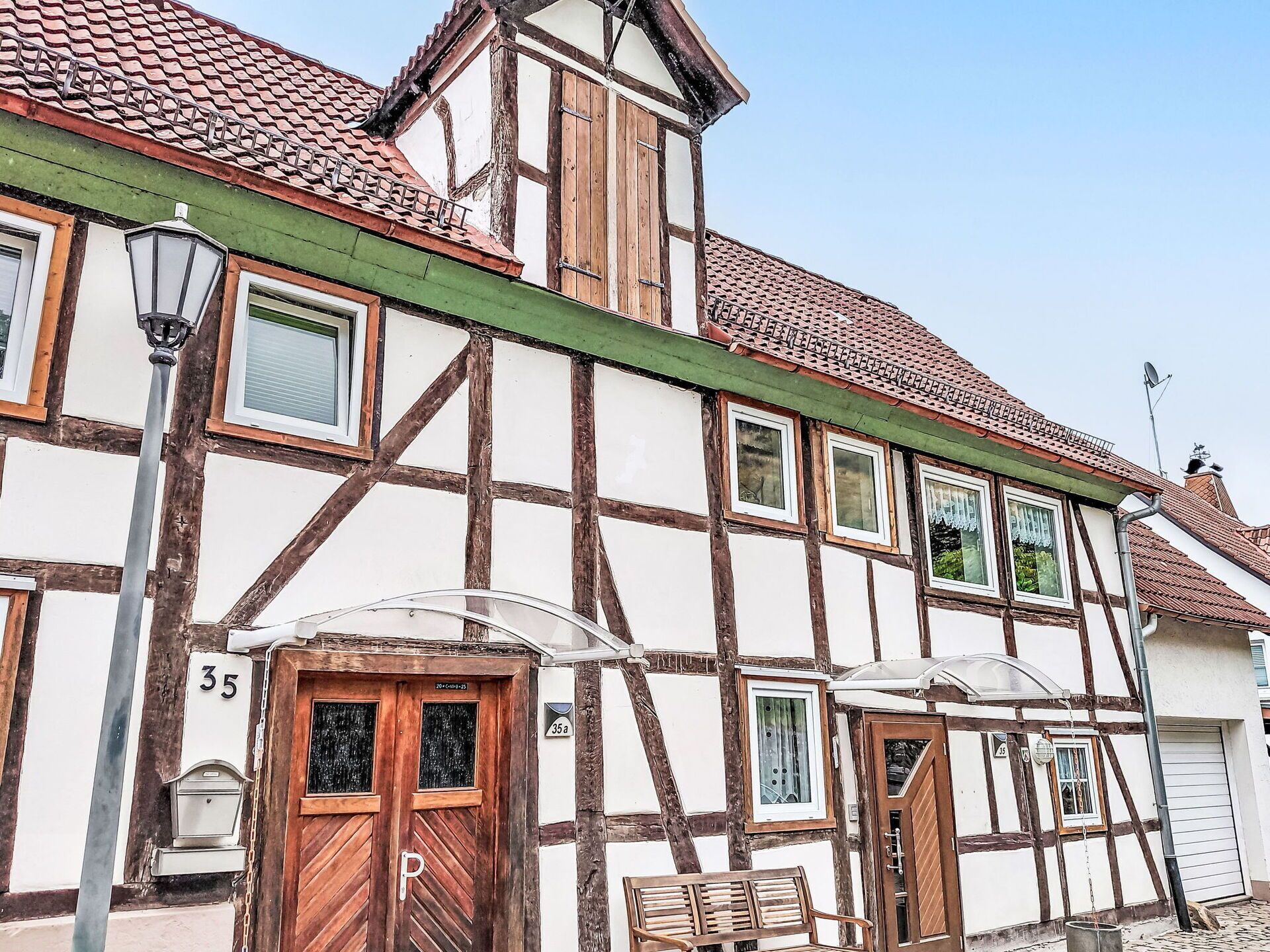 Ein traditionelles Fachwerkhäuschen mit einem grünen Dach, einer Holztür, die mit einem 'P' gekennzeichnet ist, und einer Bank vor der Tür.